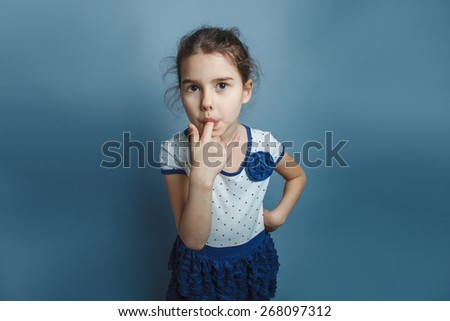 European-looking girl five years his finger in his mouth on a gray background
