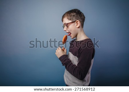 boy teenager European appearance in sunglasses licks candy bright candy on a gray background, happiness, profile