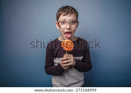 boy teenager European appearance in sunglasses licks candy bright candy on a gray background, happy, sweet