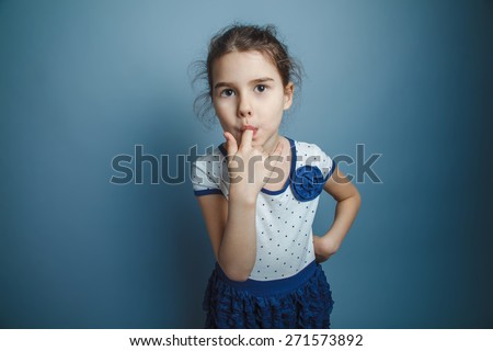 a girl of seven European appearance brunette stuck his index finger in his mouth on a gray background, licking, sucking thumb