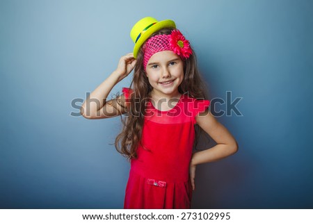 Girl European appearance haired child of seven years in a bright yellow dress hat smiling on a gray background