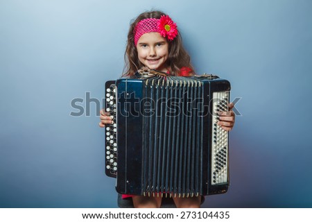 girl seven years of European appearance with a bright-haired child playing on a hairpin akardeone on a gray background, music