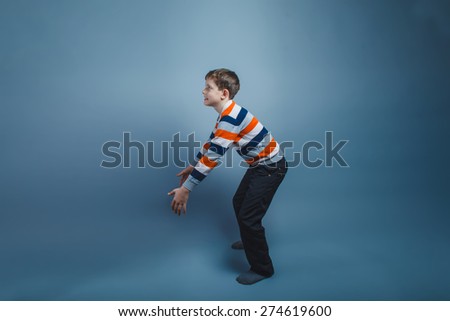 teenager boy standing European appearance on the floor stretched out his hands forward on a gray light background, catching the object
