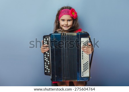 teen girl of European appearance five years holds the accordion in her hands on a gray background