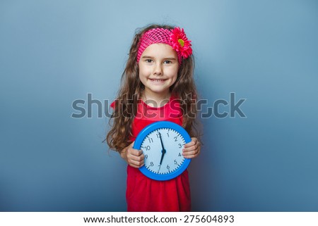 teen girl of European appearance five years holds in the hands of a wall clock on a gray background