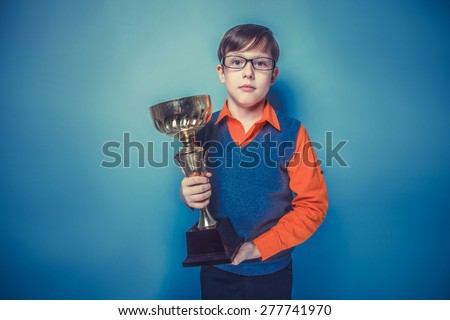 European-looking  boy of  ten years in glasses holding a cup, award joy on a blue background instagram effect style