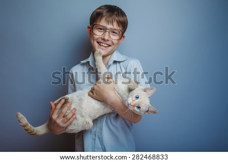 A boy of about ten European appearance in light brown shirt and glasses holding a cat with bright blue eyes on a gray background, animal, love