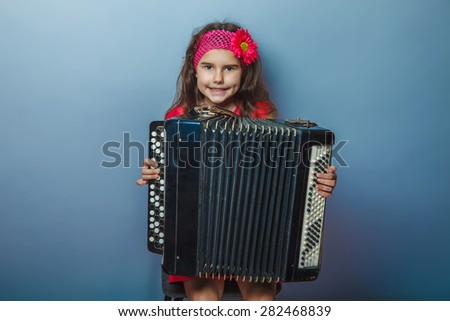 a girl of seven European appearance brunette in a bright dress plays accordion on a gray background, music, talent