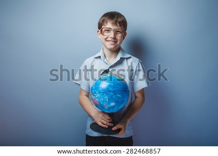 baby boy of ten European appearance in a light brown shirt and glasses holding a globe and smiling on a light background
