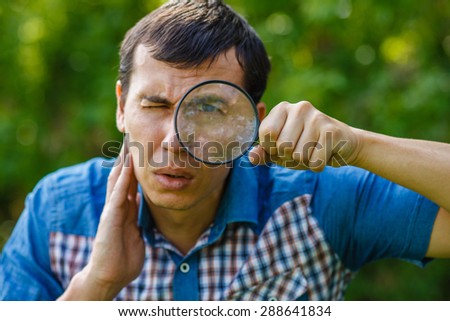 The man in the street holding a magnifying glass big eyes on a green background  leaves  summer