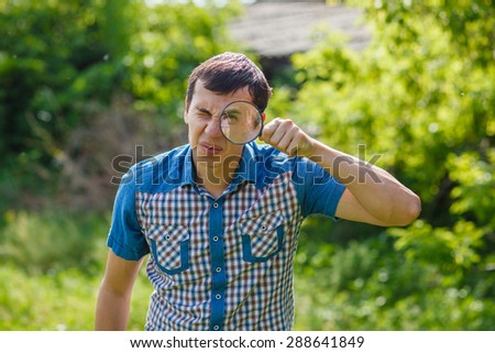 The man in the street holding a magnifying glass big eyes on a green background leaves summer