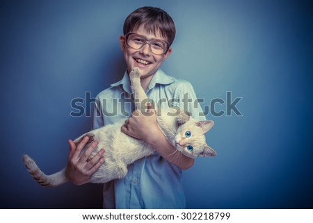 A boy of about ten European appearance in light brown shirt and glasses holding a cat with bright blue eyes on a gray background, animal, love retro photo effect
