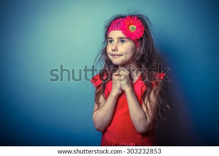 a girl of seven European appearance brunette praying, religion in a bright dress folded her hands in prayer on a gray background, faith, smile retro photo effect