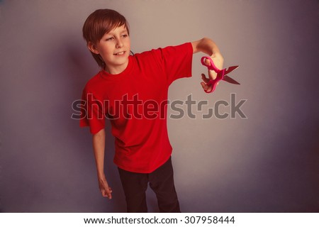 Boy, teenager, twelve years in the red shirt red is holding of pair of scissors retro