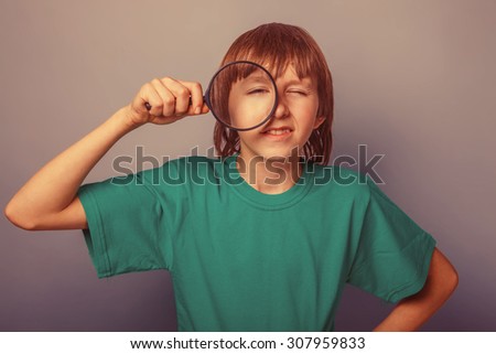 boy teenager European appearance brown hair in a shirt looking through a magnifying glass eye on a gray background, curiosity retro