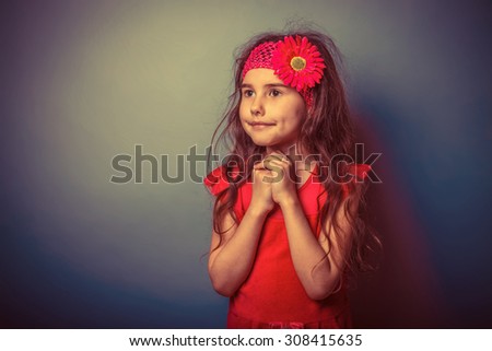 a girl of seven European appearance brunette in a bright dress folded her hands in prayer on a gray background, faith, smile retro