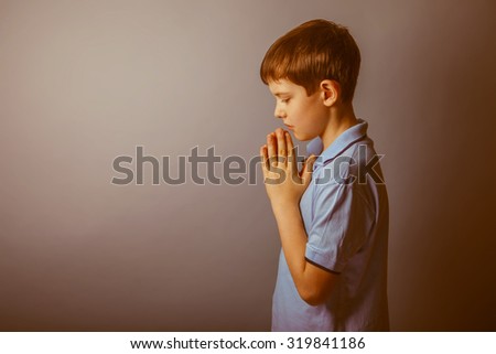 boy teenager European appearance in a blue shirt brown hair hung his head closed his eyes on a gray background, prayer retro