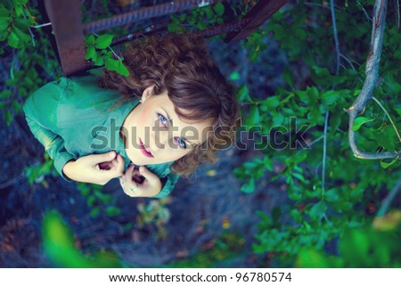 curly girl woman next to old iron stairs to nature of green background of foliage