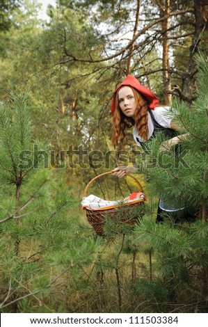Red Riding Hood with basket. The picture of Little Red Riding Hood peeking out from behind of a Pine-tree.