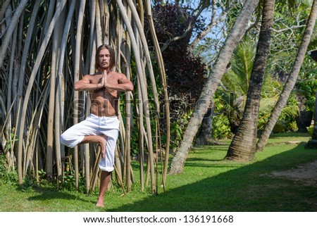Yoga. Young man in yoga position in a tropical garden.