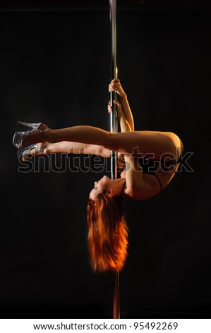 Upside-down rider. Young redhead woman hanging on a pole upside down