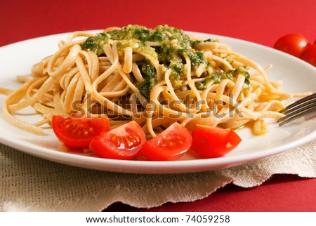 Pasta with pesto sauce with cherry tomatoes on red background