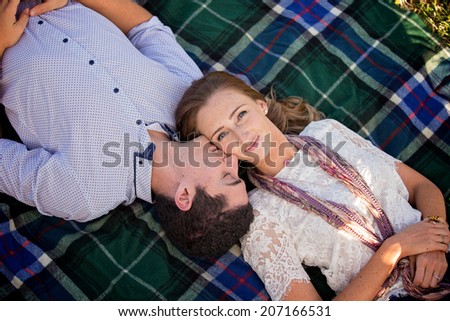a young couple lying on a rug, with male kissing cheek