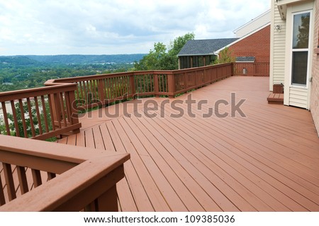 A freshly painted and stained wood deck with railing on a summer afternoon.  The deck overlooks a beautiful valley and mountains in the distance.