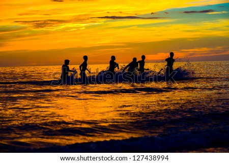 A group of boys playing football in the Gulf of Mexico at sunset.  Silhouettes against a brilliantly colored sky and water.