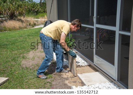 Landscaping Work - A man working outdoors.  He is placing concrete patio slabs in the landscaping near the door to the house.