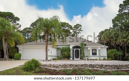 Typical Southwest Florida concrete block and stucco home in the countryside with palm trees, tropical plants and flowers and pine trees.