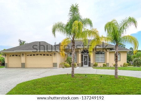 Typical Southwest Florida concrete block and stucco home in the countryside with palm trees, tropical plants and flowers, a bahia grass lawn and pine trees.