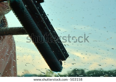 Window Washing - Image of a man washing the windshield of his car. Shows the sky in the background and water beads on the windshield.