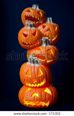 Jack O Lanterns - a stack of pumpkins carved into lighted jack-o-lanterns over deep blue background for Halloween.