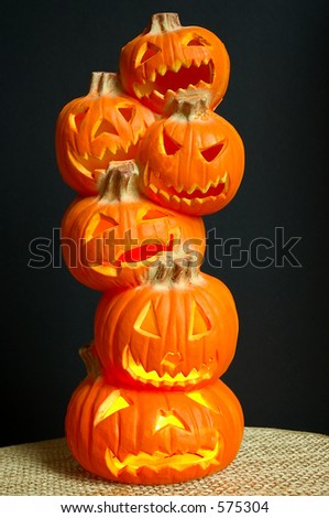 Jack O Lanterns - a stack of pumpkins carved into lighted jack-o-lanterns sitting on a straw mat with black background for Halloween.