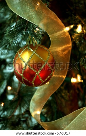Christmas Tree - Red and gold holiday ornaments and golden ribbon garland hang from the  branches of a lighted Christmas tree.