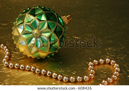 Green and gold ornament and gold beads on gold reflective, embossed paper.
