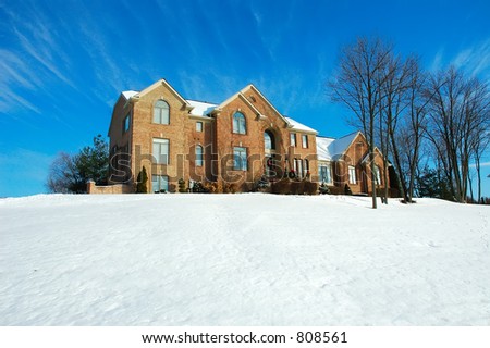Three story brick American house sitting on a snow covered hill in winter under a brilliant deep blue sky.  Decorated for the Christmas holiday season.