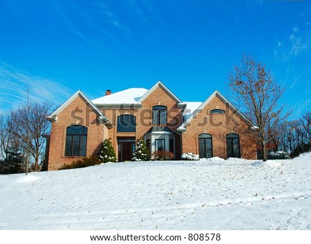 Two story brick American house sitting on a snow covered hill in winter under a brilliant deep blue sky.