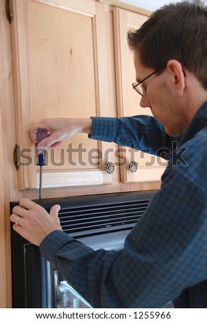 Man using a screwdriver to repair his microwave in the  kitchen of a modern home.