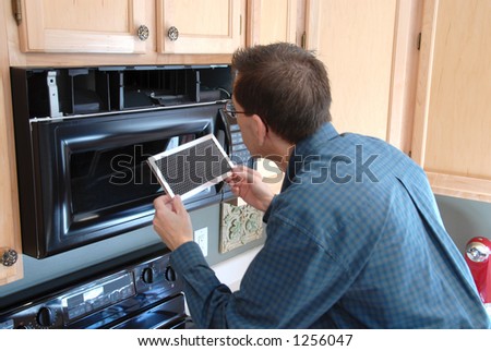 Man replacing the filter in a microwave in the kitchen of a modern home.