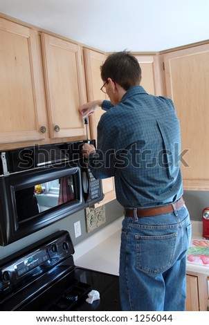 Man using a screwdriver to repair his microwave in the  kitchen of a modern home.