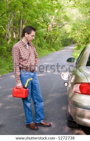 Upset man holding a gas can on a country road, staring at the empty gas tank of his car.