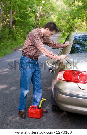 Upset man on a country road, staring at the empty gas tank of his car with a gas can at his feet.