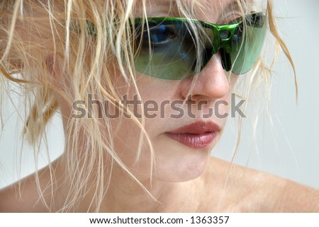 A blonde woman with messy hair, wearing no makeup other than lipstick, hiding behind green sunglasses and looking to the side.  Bad hair day.