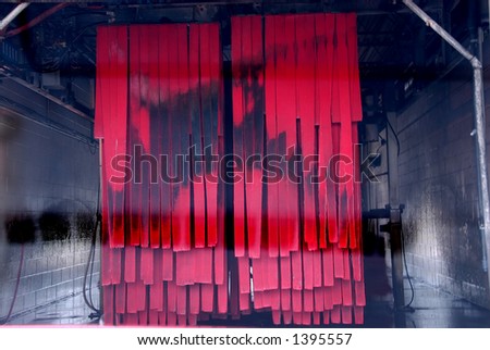 Entering the soft cloth car wash tunnel before the automatic system starts spraying.  Interior of the car wash viewed from inside the car.  The red cloths are hanging with black grime on them.