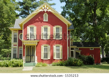 Red Farm House - An old farmhouse in the country with red siding and cream colored shutters and gingerbread trim sits in the shade  of huge trees.