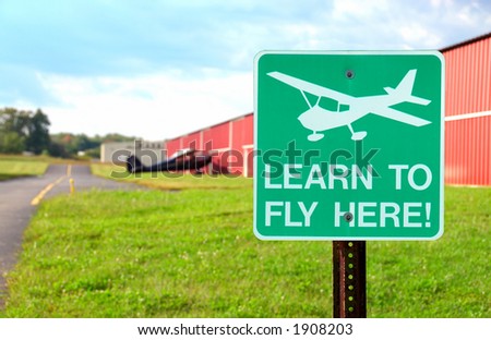 Airport Sign - Learn To Fly Here - a sign in front of the hangars at a small airport .