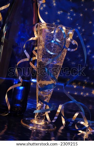 New Year Toast - Crystal champagne flute and blue bottle of wine against a brilliant blue starry background.