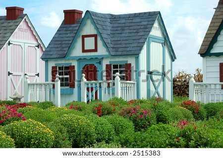 Gingerbread Houses in a Row - A row of small storage or garden sheds that look like play houses sit in a garden of mums in the springtime.